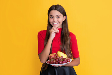 positive kid hold fresh fruit plate on yellow background