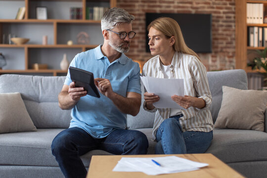 Worrying busy sad middle aged european lady with documents and male with tablet work with bills