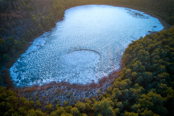 Aerial view of frozen lake. Frozen lake surrounded by trees. Winter sunset over frozen lake 