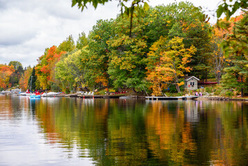 Adirondack chairs on wooden jetties along the forested bank of a river on a cloudy autumn day. Stunning autumn colours.