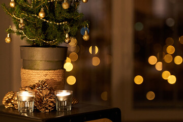 Natural Christmas decor. Small Christmas tree by candles and golden pine cones