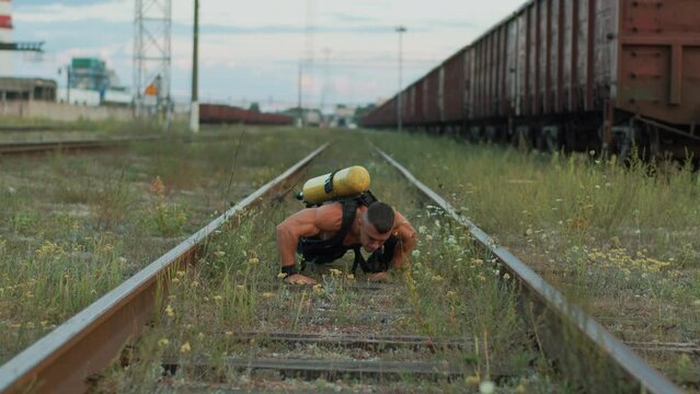 Young muscular man with balloon drager on his back training at marshalling yard and moves on arms and legs between the rails