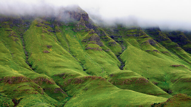 Dramatic view on the green mountains of Drakensberg with fog in the peaks in the morning in South Africa