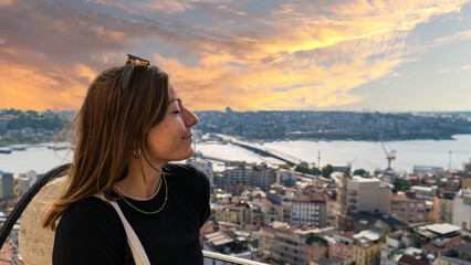 Fototapeta na wymiar Young tourist woman sightseeing with Istanbul landscape at sunset. Young beautiful woman watching Istanbul from the Galata Tower