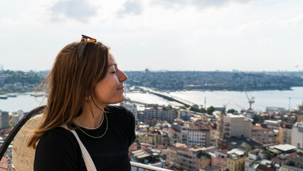Naklejka premium Young tourist woman sightseeing with Istanbul landscape at sunset. Young beautiful woman watching Istanbul from the Galata Tower