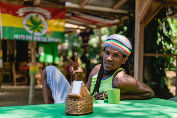 Retrato horizontal de un hombre afrocaribeño sonriente con cabello rasta sentado solo en el...