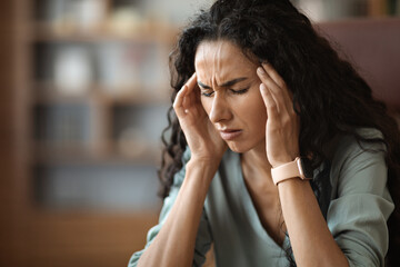 Upset young woman suffering from headache while working