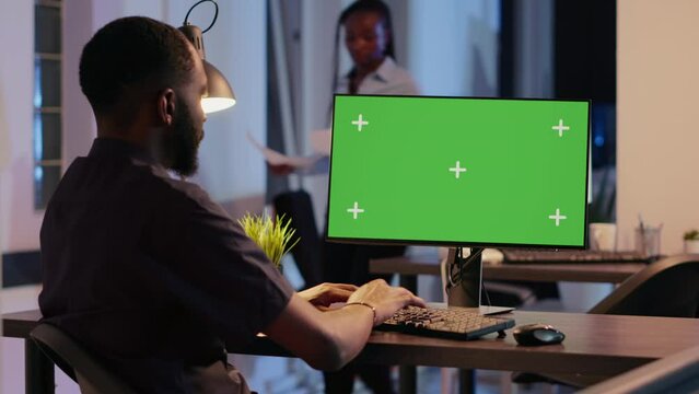 Office employee working with greenscreen display on computer late at night. Looking at isolated copyspace background with blank mockup and chroma key template on monitor screen.