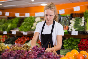 Portrait of teenage girl working in grocery shop as job experience, selling fresh grape