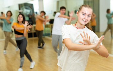 Fototapeta na wymiar Cheerful teen girl enjoying while training movements of modern group dance in choreography class .