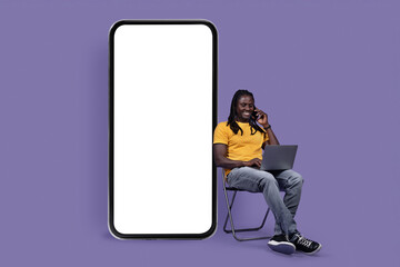 Happy handsome black guy working on purple, having phone call