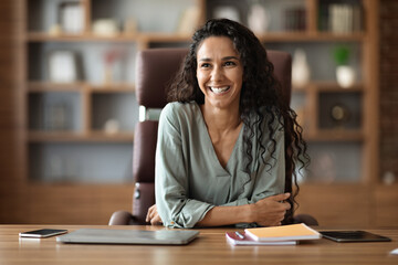 Cheerful young woman posing at workdesk at office, copy space