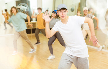 Portrait of expressive teenage krump dancer in choreographic studio with dancing teenagers in background. Typical Generation Z .