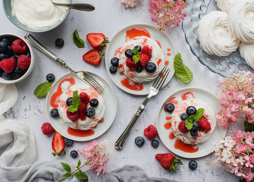 Overhead of mini pavlova meringue cakes with fresh berries and cream.