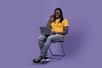 Young black man freelancer working on laptop, having phone call