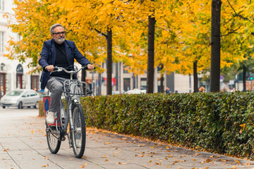 Full-length outdoor shot. Business-casual looking caucasian man in eyeglasses happily cycling through his favorite city park where trees are changing the color of their leaves. High quality photo - Powered by Adobe