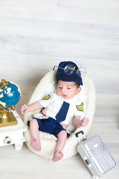 toddler boy in pilot uniform sitting at soft tiny chair,toy suitcase world map,face photography