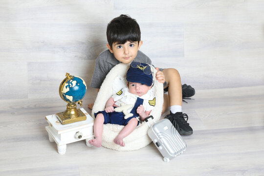 toddler boy in pilot uniform sitting at soft tiny chair with elder brother, toy suitcase world map