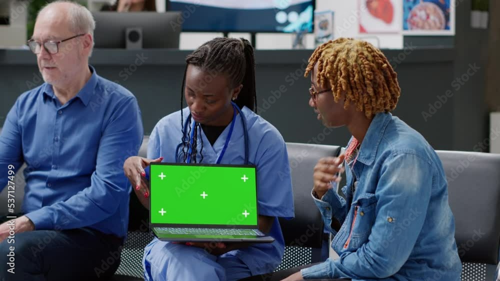 Poster medical assistant showing laptop with greenscreen to young patient in waiting room lobby. using blan