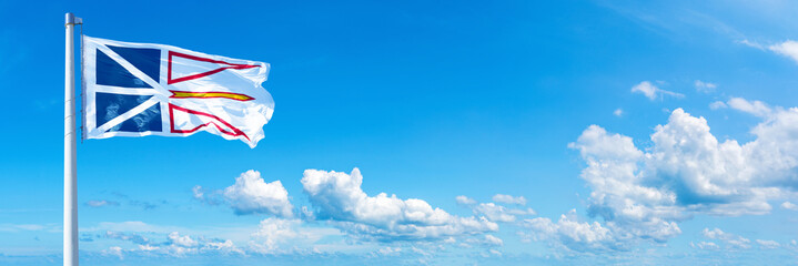Newfoundland and Labrador - Canada flag waving on a blue sky in beautiful clouds - Horizontal banner
