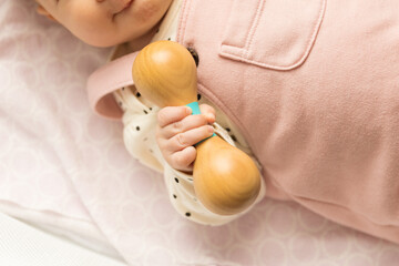 Baby holding a wooden rattle toy - obrazy, fototapety, plakaty