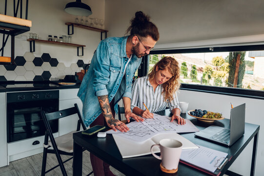 Happy couple using laptop and looking into blueprints of their new home - Powered by Adobe