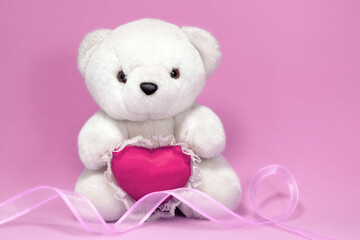 White bear with heart and pink ribbon, symbol of pink autumn. Campaign against breast cancer. Pink background, space for writing.