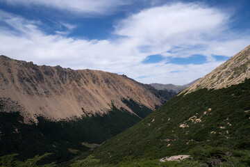 Alpine landscape. Hiking in the mountains. Panorama view of the hills, valley and forest under a beautiful sky with clouds. 