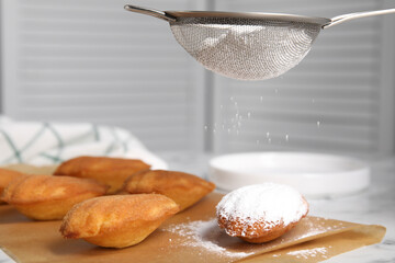 Decorating delicious madeleine cakes with powdered sugar on table, closeup