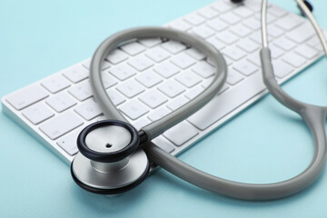 Computer keyboard with stethoscope on turquoise background, closeup