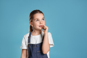 Cute little girl biting her nails on turquoise background, space for text