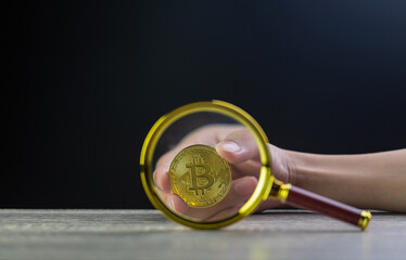 Virtual money silver bitcoin under a magnifying glass on the background of heap of coins in hand.