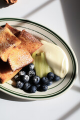 French toast with blueberries, kiwi and cream on white plate under sunlight. Morning coffee breakfast. French breakfast.