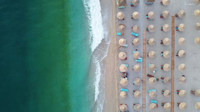 Aerial shot of beach waves with sunbed and thatch umbrella rows on the sand