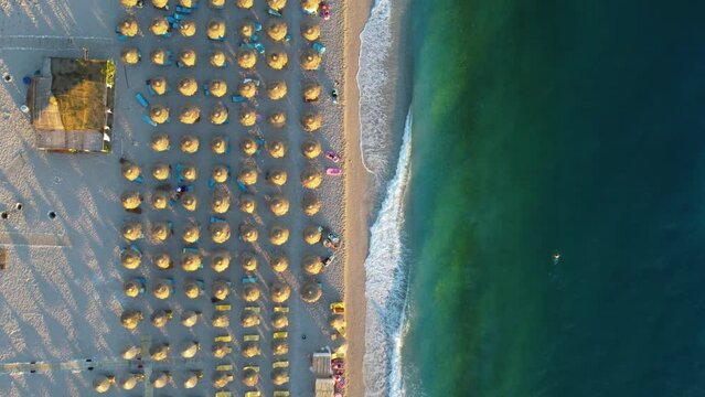 Aerial shot of the beach waves and thatch umbrella rows on the sand