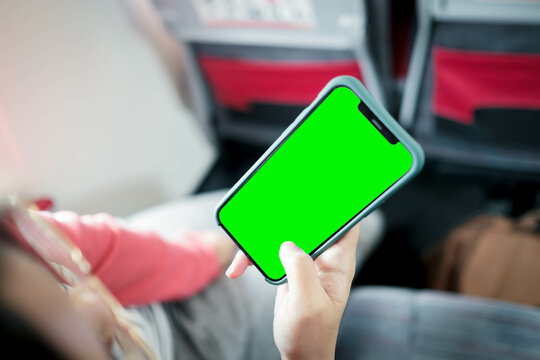 Mockup image of a business people holding smart mobile phone with blank green screen  on board of airplane near window seat and wing with countryside background.