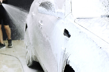 Man washes a brown car at a car wash. Coated with car foam. Close-up of the front fender with...