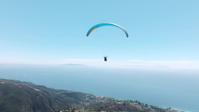 Extreme paraglider flying in clear blue skies, toward cinematic teal ocean. Woman with instructor flies with paraglide 4k. Cinematic aerial drone footage above Malibu USA slow motion up in the air