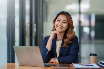 Happy young asian businesswoman sitting on her workplace in the office. Young asian woman working at laptop in the office.