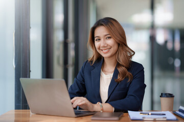 Fototapeta premium Happy young asian businesswoman sitting on her workplace in the office. Young asian woman working at laptop in the office.