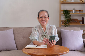 Fototapeta na wymiar Asian senile woman relaxing at home using mobile phone in living room playing social media on vacation.