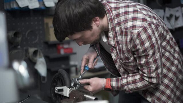 Handyman fixes a wheel from a scooter clamped in a clevis and twists it with a crescent wrench in the shop. Repairman uses a adjustable wrench to repair a part of a children's bicycle in the workshop.