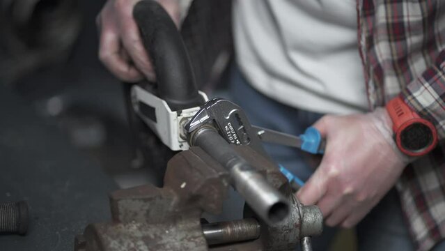Handyman fixes a wheel from a scooter clamped in a clevis and twists it with a crescent wrench in the shop. Repairman uses a adjustable wrench to repair a part of a children's bicycle in the workshop.