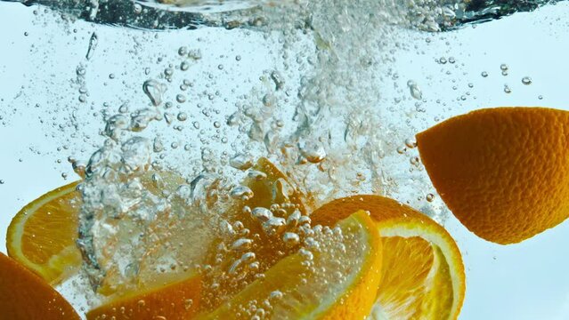 Orange wedges splashing water in super slow motion close up. Citrus underwater.