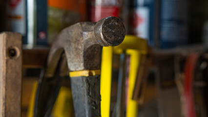 Martillo de hierro acero colgado en una repisa de herramientas, con mango de goma de color negro y amarillo , rodeado de herramientas y latas de pintura