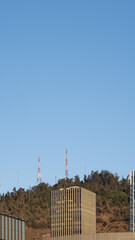 Fototapeta premium Vista de un edificio con cielo azul. De fondo un cerro con antenas de comunicación