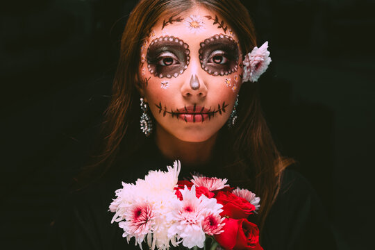 High quality photography. Young woman with painted skull on her face for Mexico's Day of the Dead against dark background. Mexican catrina. Woman personified as catrina on the day of the dead.