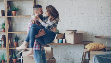 Happy strong man is whirling his excited wife and kissing her during relocation to new house after...