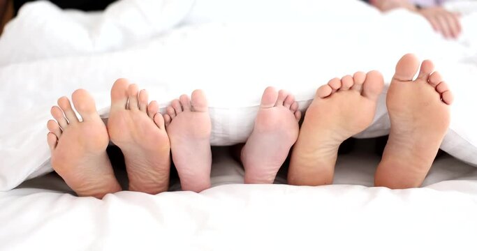 View of legs of unrecognizable family located next to each other in bed