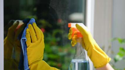 Female hands cleaning window outside using detergent spray and rag